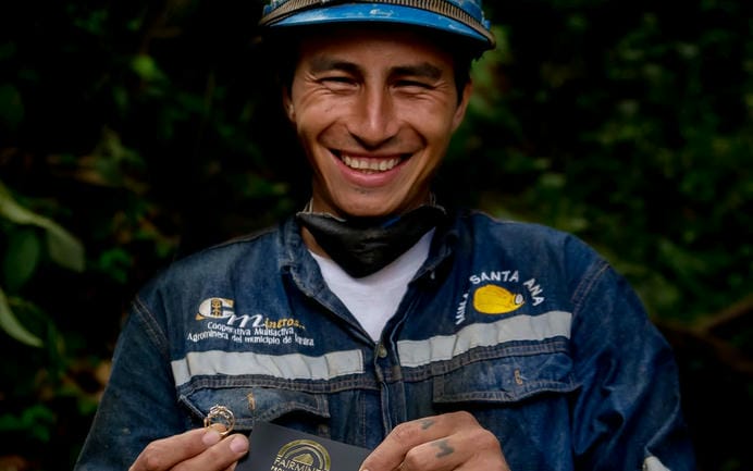 Man smiling looking into the camera wearing Fairmined branded miners blue overall and helmet.