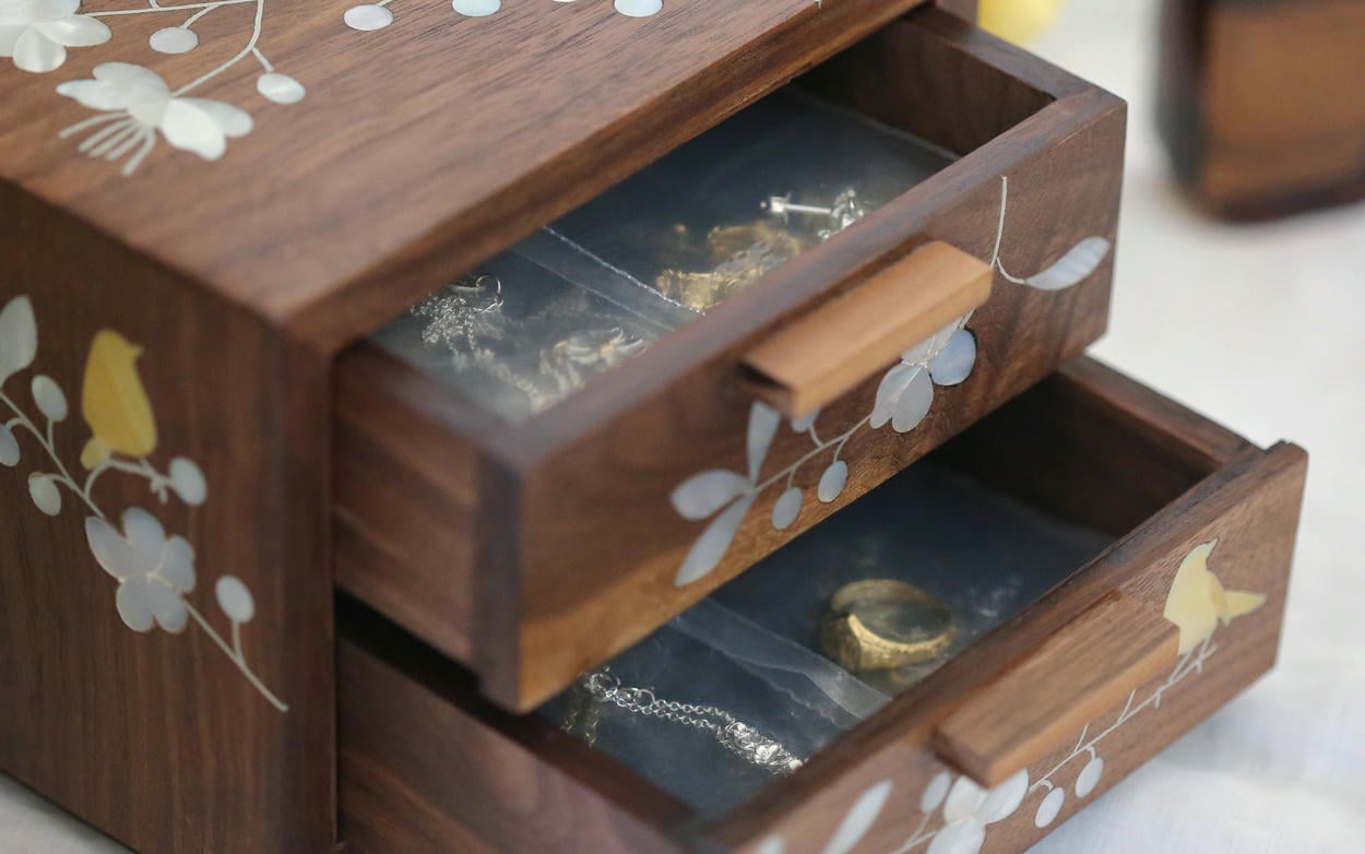 Wooden jewellery box with mother of pearl floral and bird details, with 2 open drawers containing jewellery stored in small ziplock clear plastic pouches.