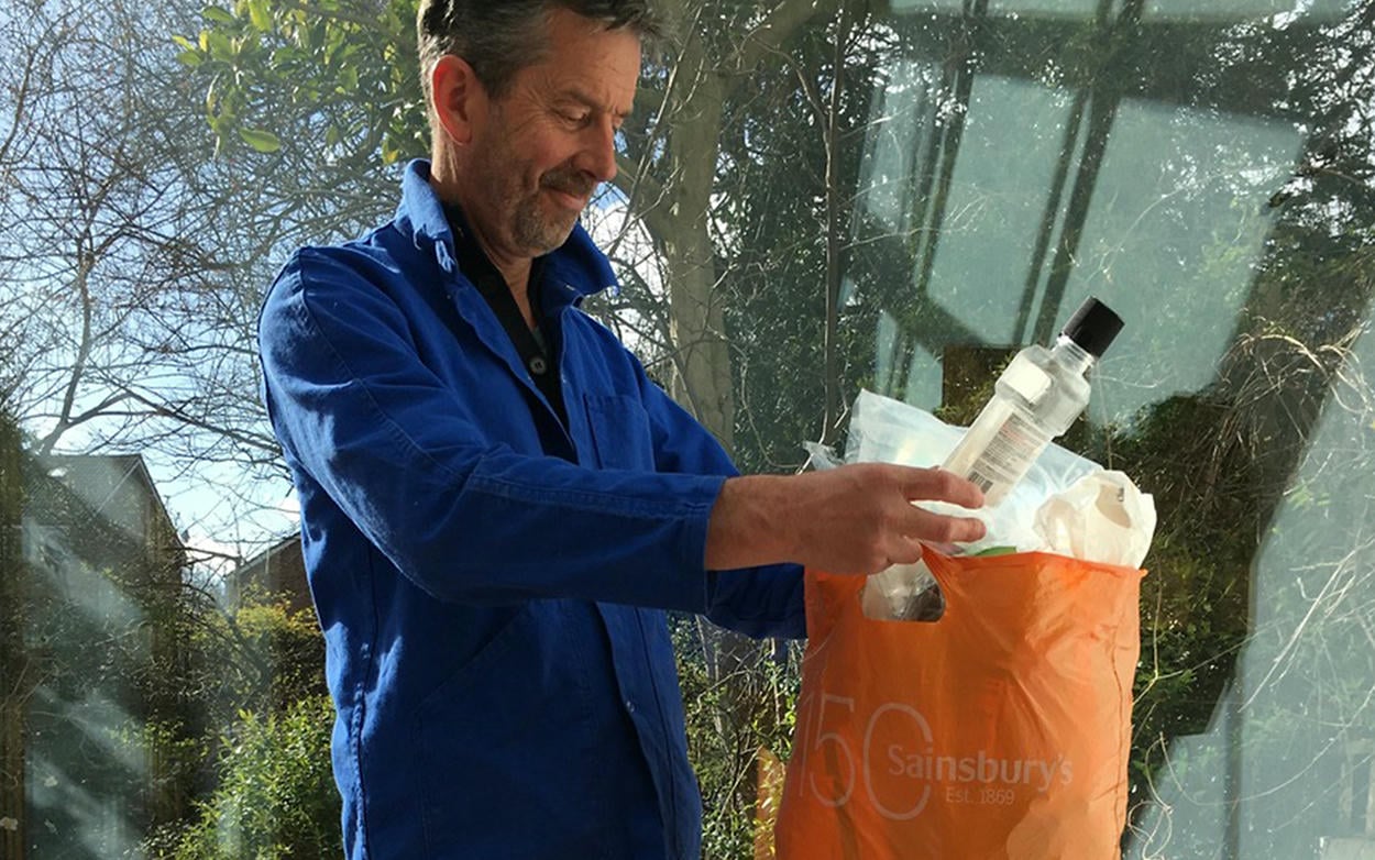 Alex Monroe collecting single use plastic bottles and food packaging in an organge bag for life.