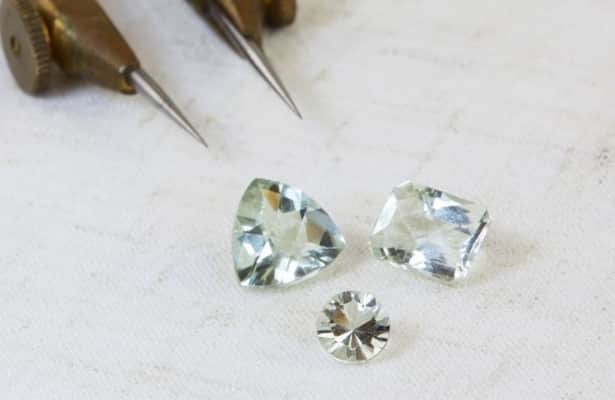 Three pale blue Amethyst gemstones scattered on a white surface.
