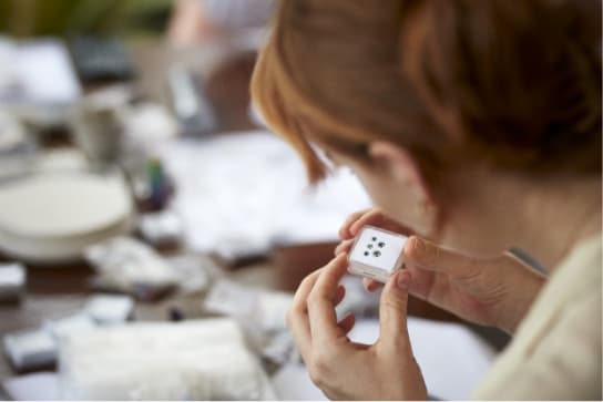 Amy looking at a small clear box holding five newly cut soft blue coloured Sri Lankan sapphires.