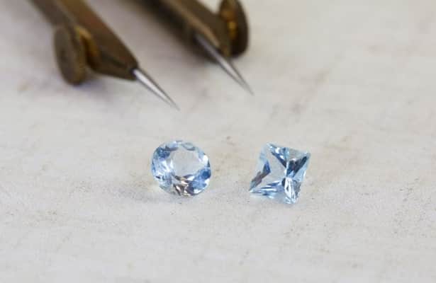 Two blue Aquamarine gemstones scattered on a white surface.