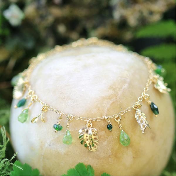 Silver charm bracelet with tropical eaves and an array of green peridot gemstones.