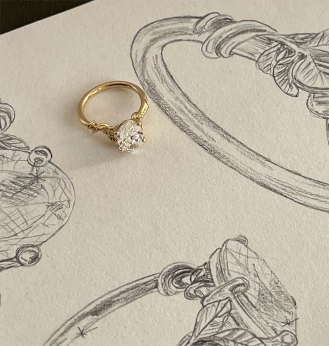 Large diamond vine leaf yellow gold ring on a piece of paper with pencil design sketches of the ring.