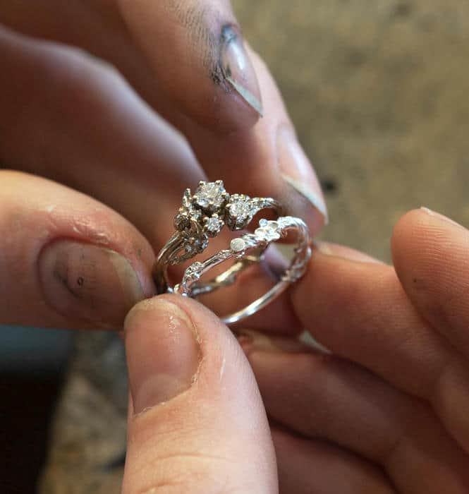 Jeweller holding a white gold trilogy diamond engagement ring next to an unfinished bespoke floral detail wedding ring.