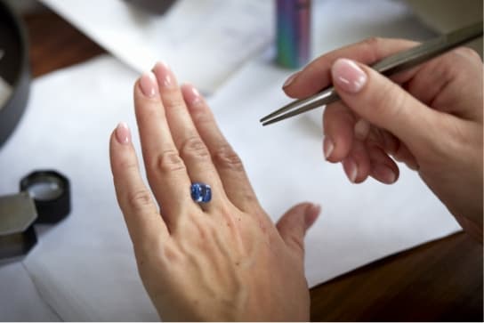 A large blue Sri Lankan mined sapphire delicately balanced on the back of a hand between third and fourth finger, being inspected in the daylight.