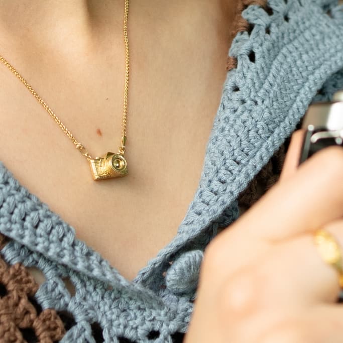Camera necklace worn with heavy knit blue and brown top