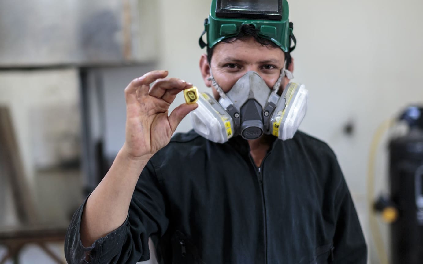 Working in overalls and respirator holding a cube of fairmined gold.