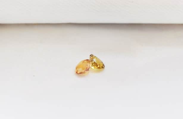Two yellow citrine gemstones scattered on a white surface.