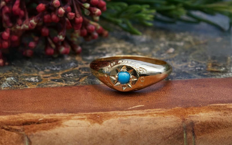Topaz gemstone star-set in a signet ring, displayed on the edge of a vintage hardback book, with red berries.