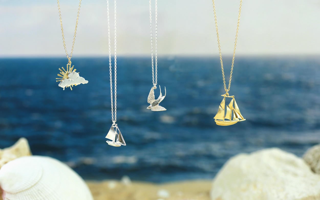 Four necklaces hanging in front of a distant ocean and beach.