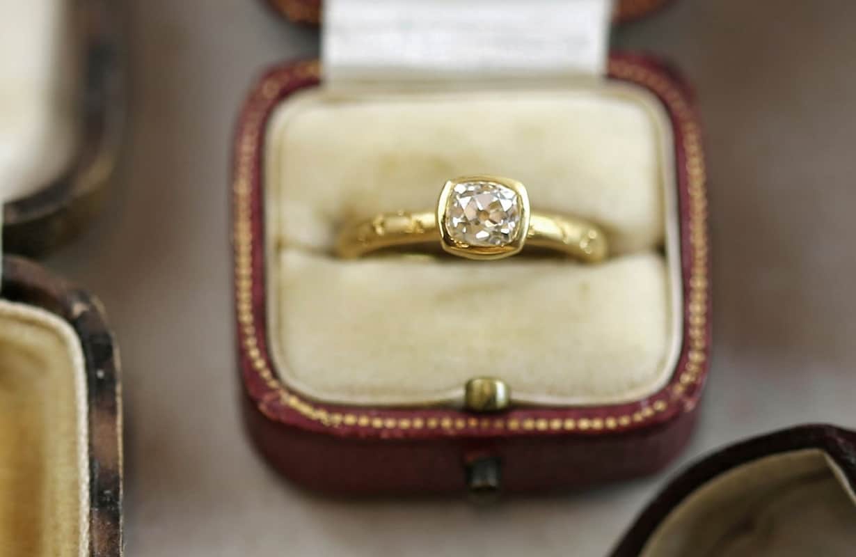 Large white antique diamond set in a textured yellow gold engagement ring, presented in a vintage ring box.