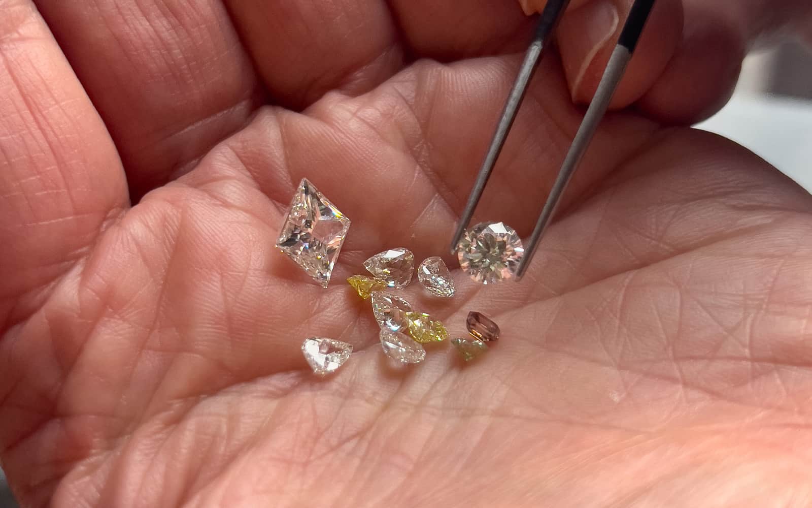 Close up of various diamonds in the palm of a hand, including yellow and champagne coloured, and different cuts, including a baguette cut and brilliant.