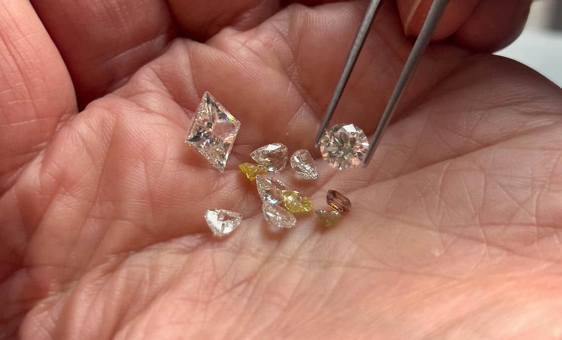 Close up of a hand holding a selection of clear, yellow and champagne diamonds.