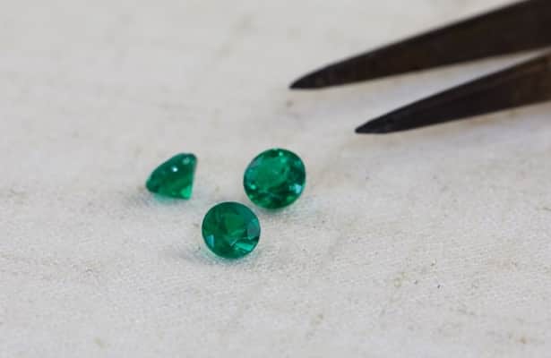 Three dark green emerald gemstones scattered on a white surface.