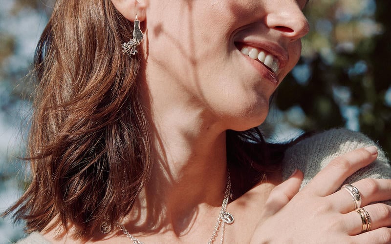 Woman smiling in dappled spring sunlight, wearing a selection of silver jewellery.