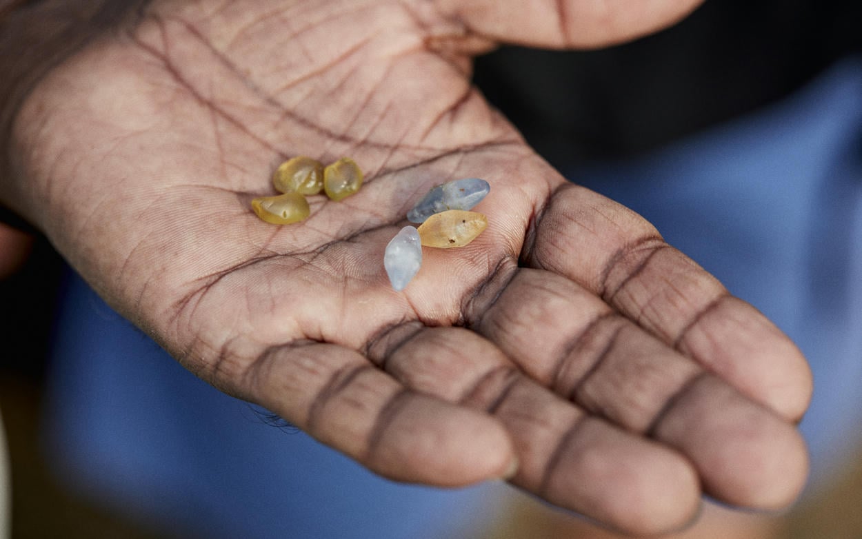 Hand held out containing a selection of raw coloured sapphires, some white, grey, and shades of yellow.
