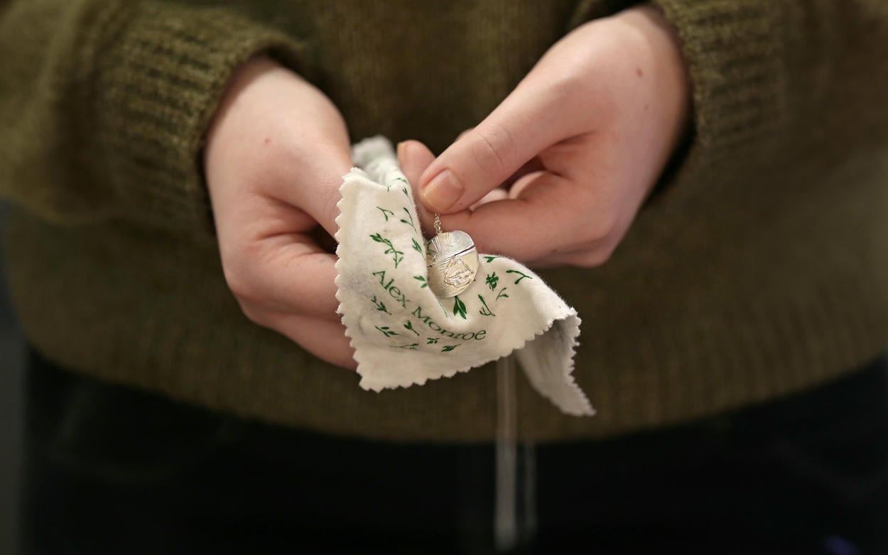 A woman cleaning a silver necklace with an Alex Monroe branded silver polishing cloth.