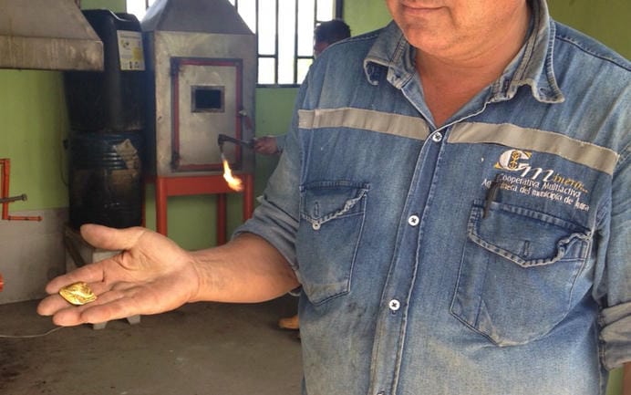 Miner holding a gold nugget in front of a metal furnace.