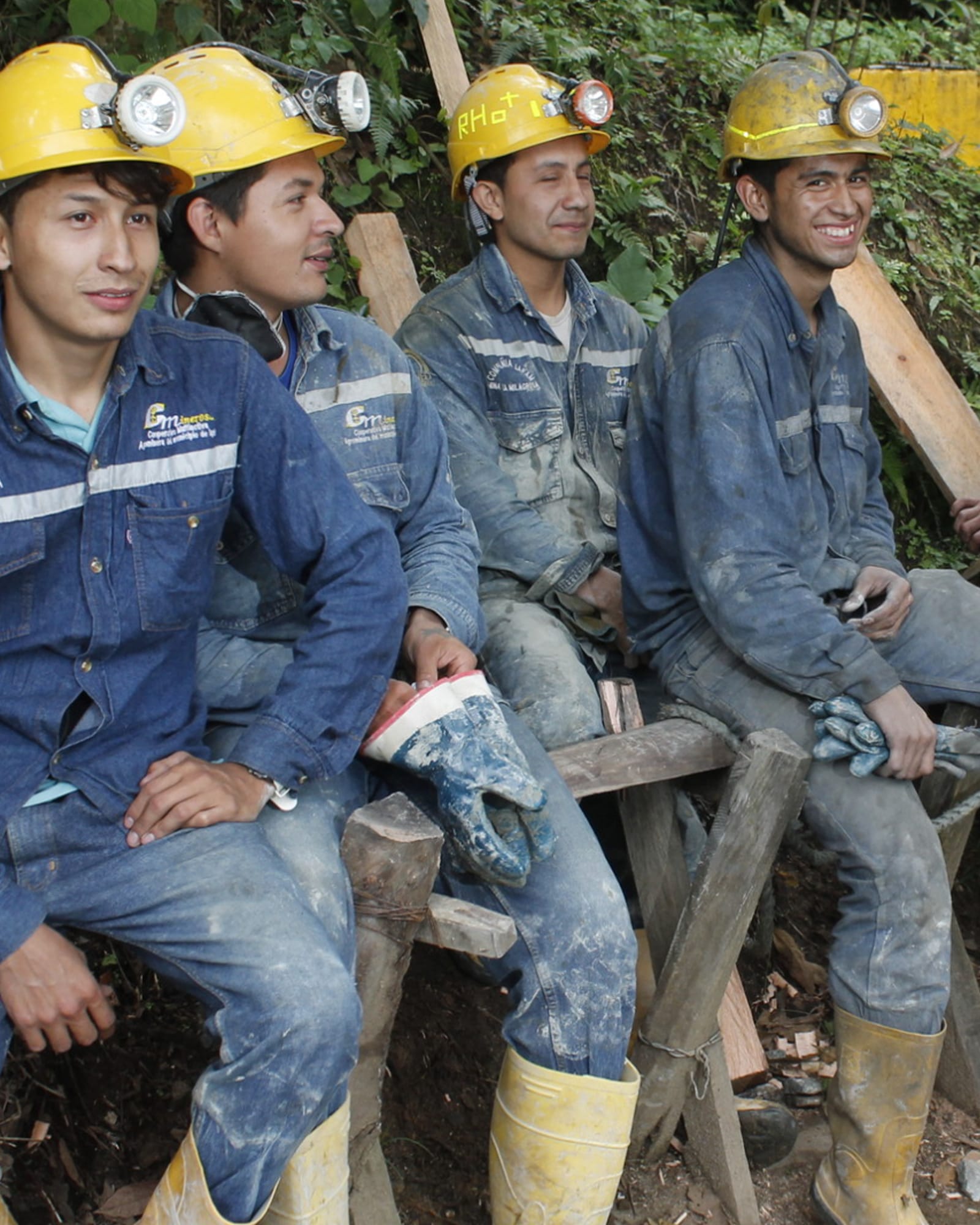 Group of gold miners in blue Fairmined overalls and helmets sitting together.