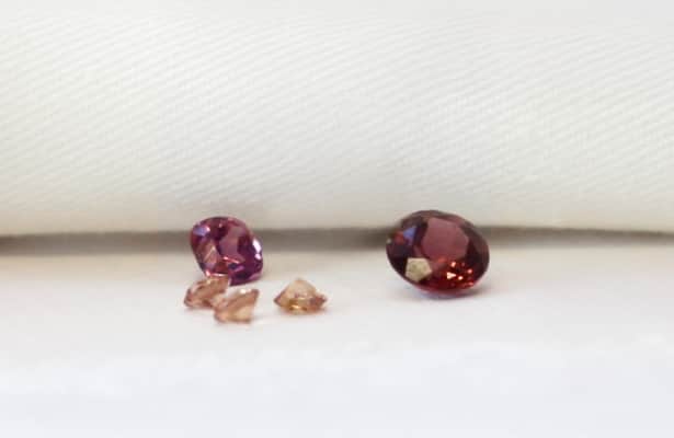 Five red garnet gemstones scattered on a white surface.