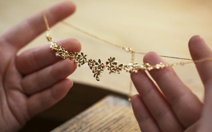 Large statement gold plated necklace being held above a jewellers bench.