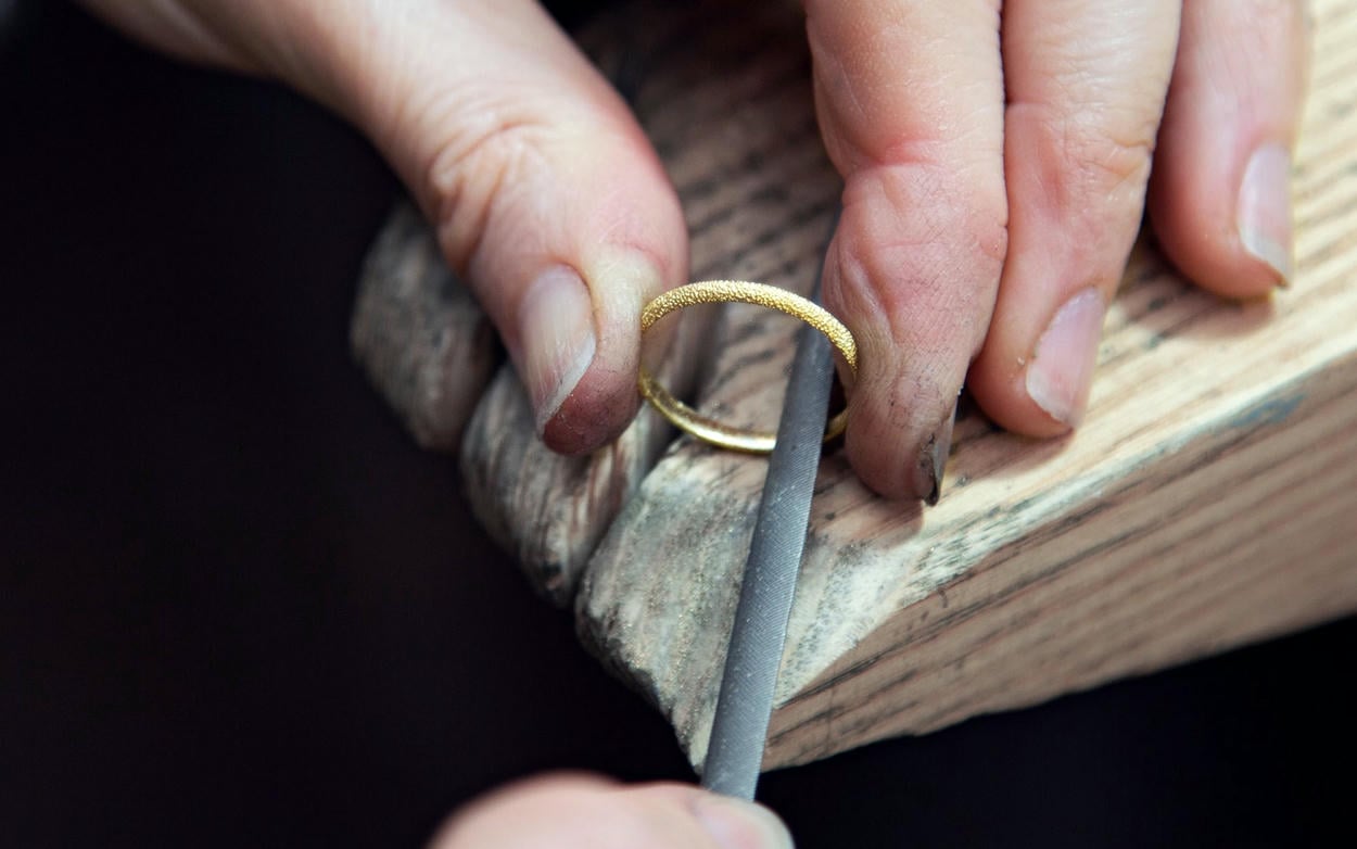 Textured solid gold ring being filed on a jewellers bench peg.