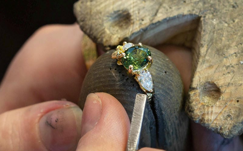 Jeweller setting diamonds and a green sapphire into a solid gold ring.