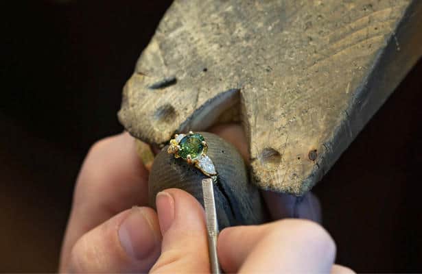 Close up of a jeweller setting a large green gemstone and 2 diamondds in an engagement ring.