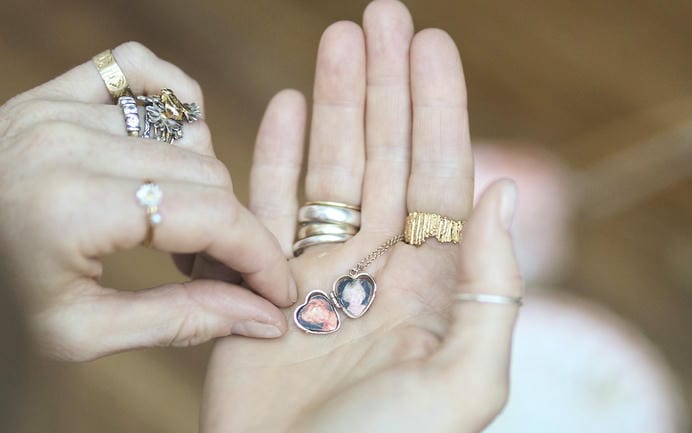 Womans hands holding a small heart locket that has been opened to reveal old photos of relatives.