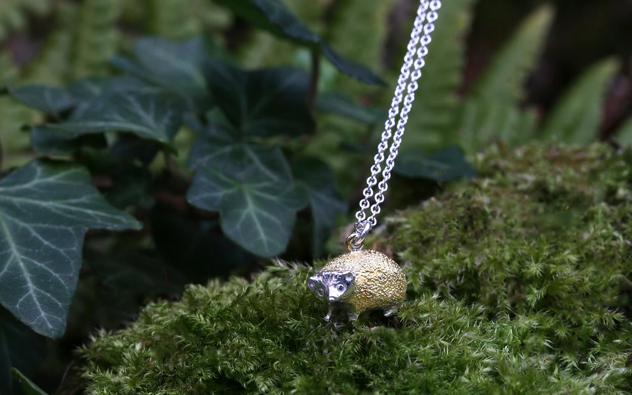 Mixed metal silver and gold plated hedgehog necklace displayed in a green mossy scene with ivy leaves.