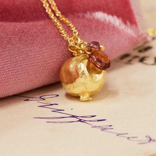 Pommegranate and garnet necklace on red fabric and parchment with cursive writing.