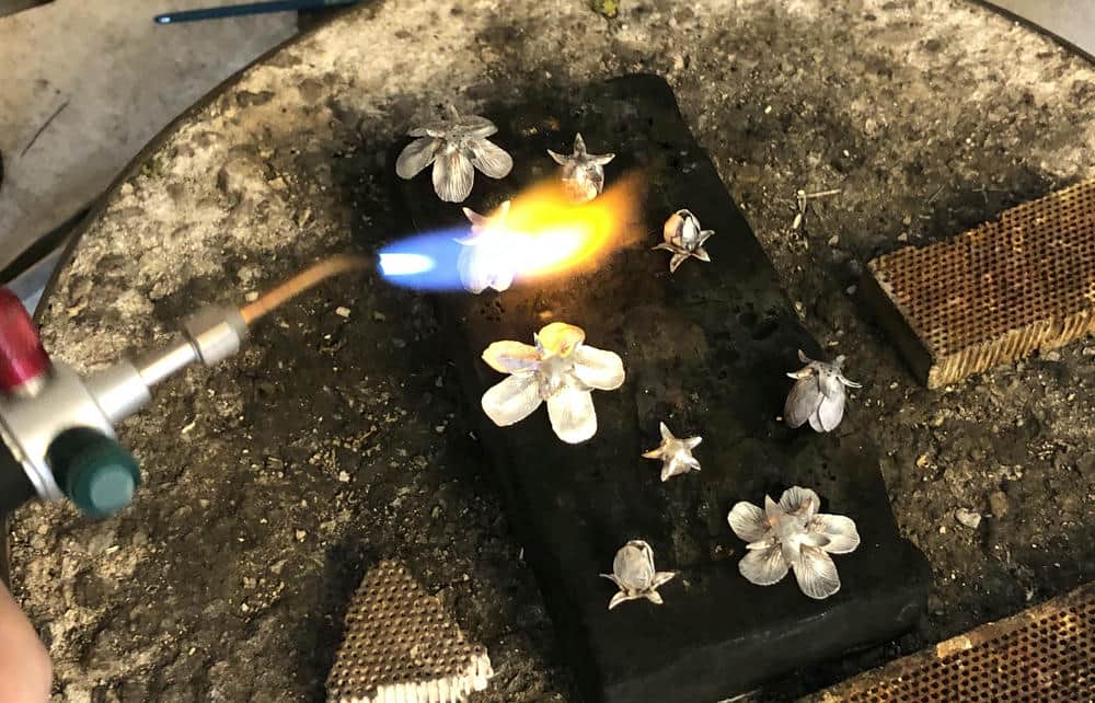 A selection of silver flower jewellery castings on a forge plate being heated up with a blowtorch.