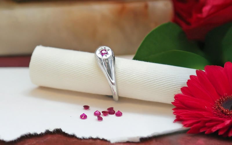 Large red flowers scattered next to a silver signet ring with star-set ruby gemstone.