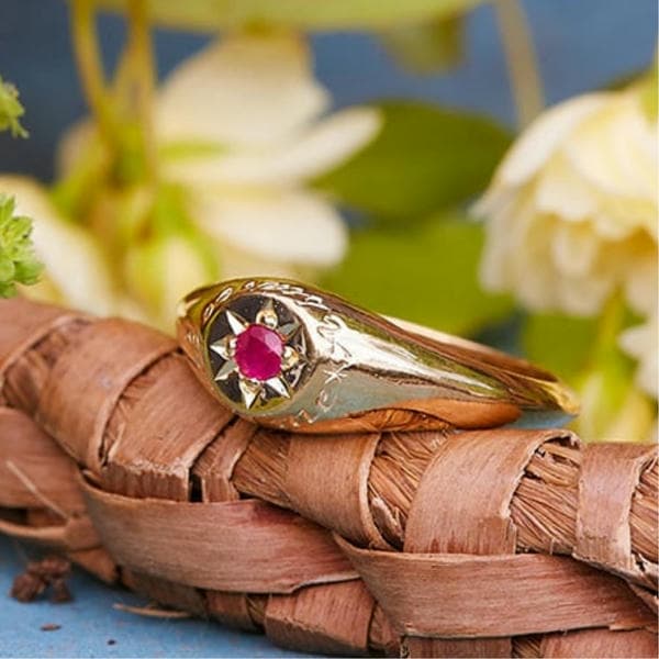 Signet ring with engraving and ruby gemstone in a star cut setting.