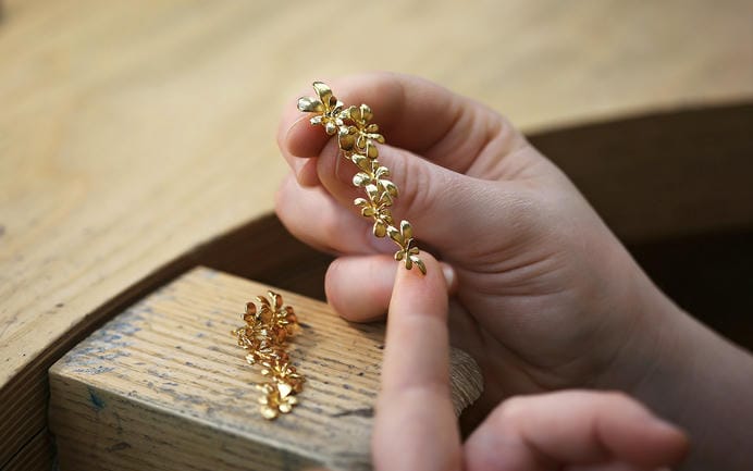 Fairmined Gold plated botanical leaf motif Alex Monroe earrings, held above jewellers bench.