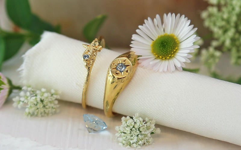 Aquamarine signet and starfish stacking ring surrounded by white daisies and smaller flowers, on a parchment scroll.