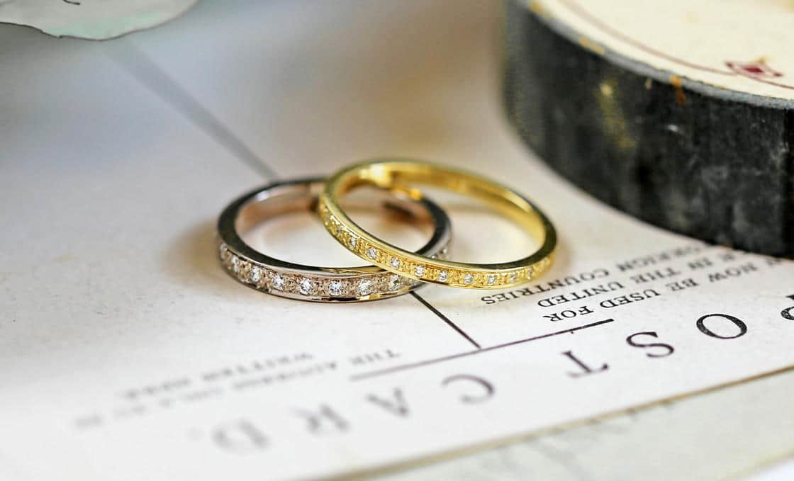 Two diamond set wedding rings, one made from white gold and one yellow gold displayed next to the edge of a vintage stationary box..