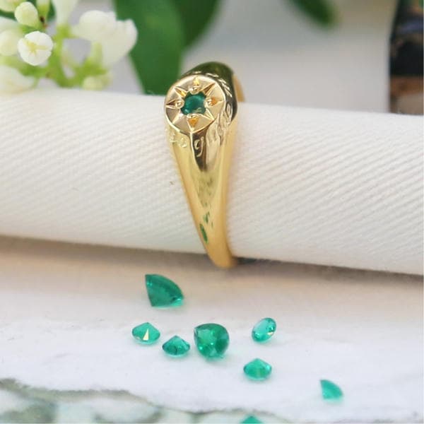 Signet Ring with star set emerald on a roll of parchment with emeralds scattered next to it.