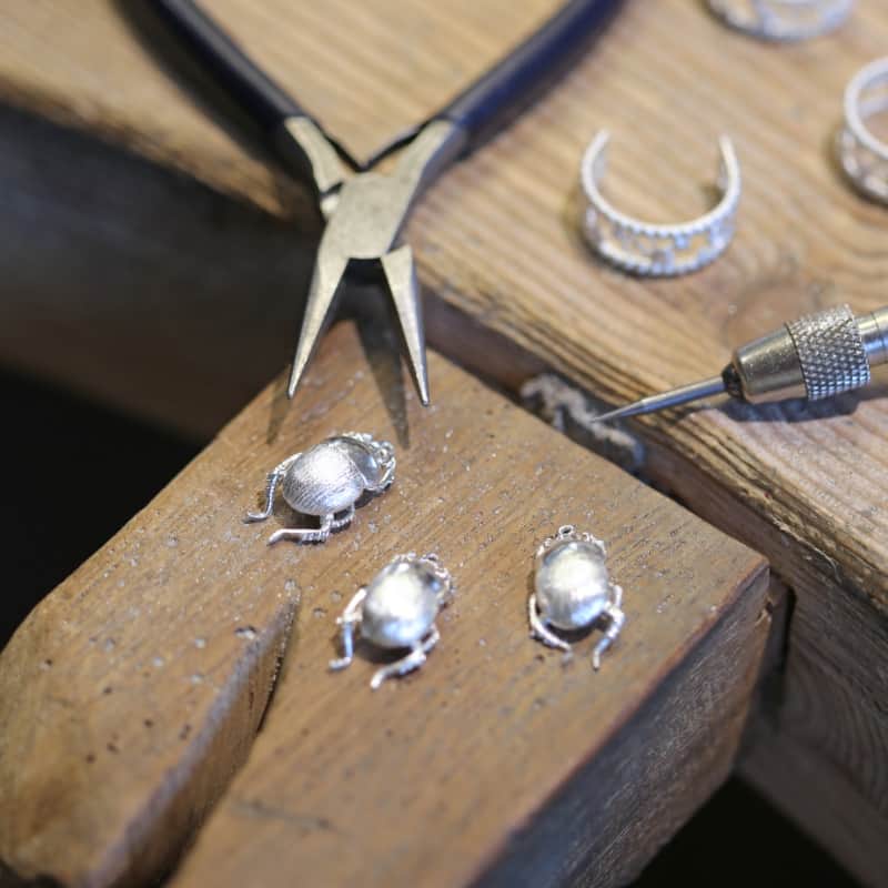 Three silver beetle castings on a jewellers workbench.