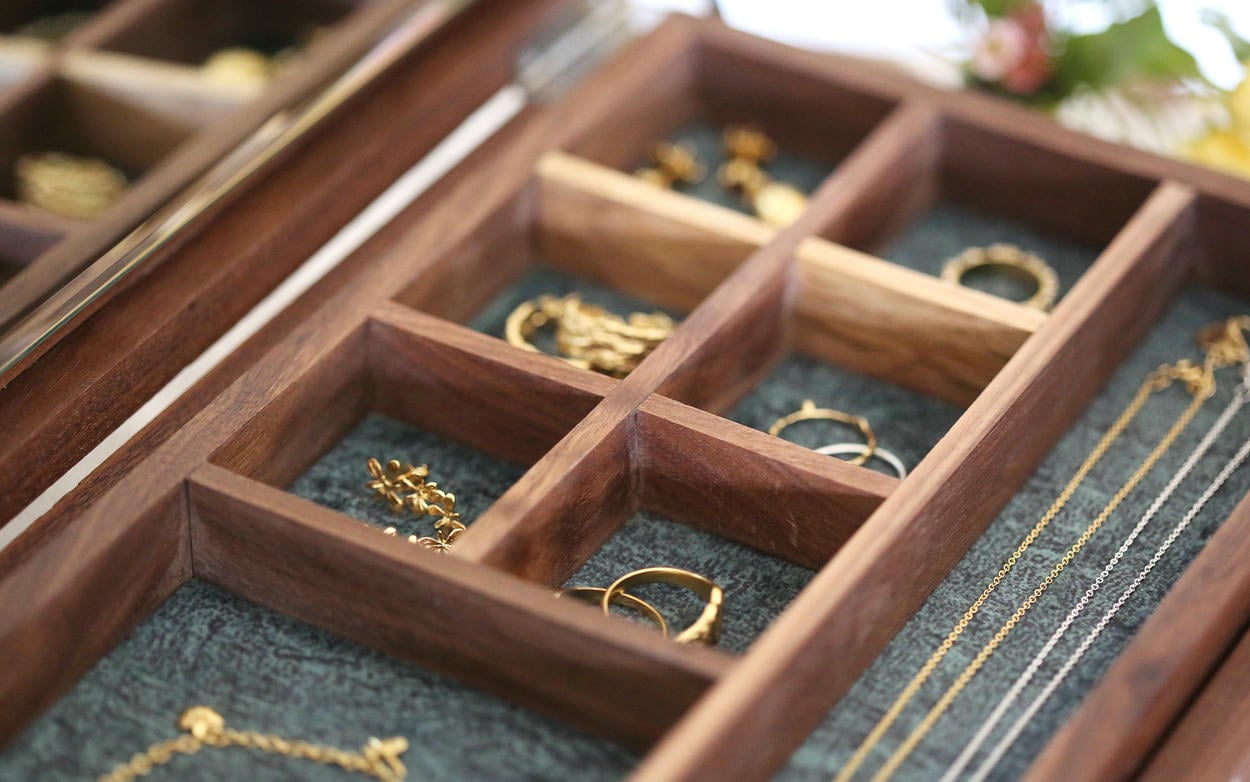 Wooden jewellery box tray with dark green felt lined compartments containing a selection of earrings, rings and necklaces.