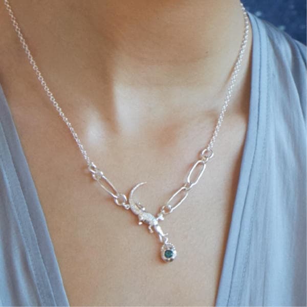 Woman in a blue blouse wearing a silver in-line necklace with short section of oversized links, a crocodile charm and set blue topaz gemstone.