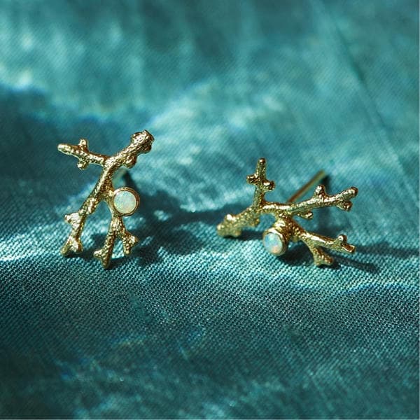 Solid gold textured coral design studs with opal gemstones on a flowing blue fabric backdrop.