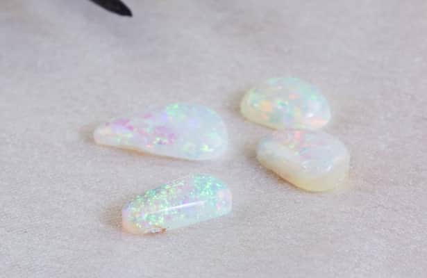 Four pearlescent opal gemstones scattered on a white surface.