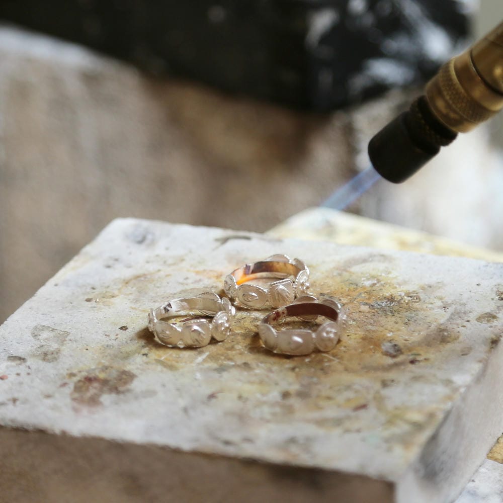 Three silver ring castings being heated by a torch on a jeweller's furnace block.