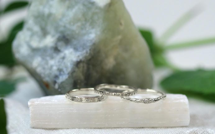 Three platinum rings arranged on a white glossy stone slab.