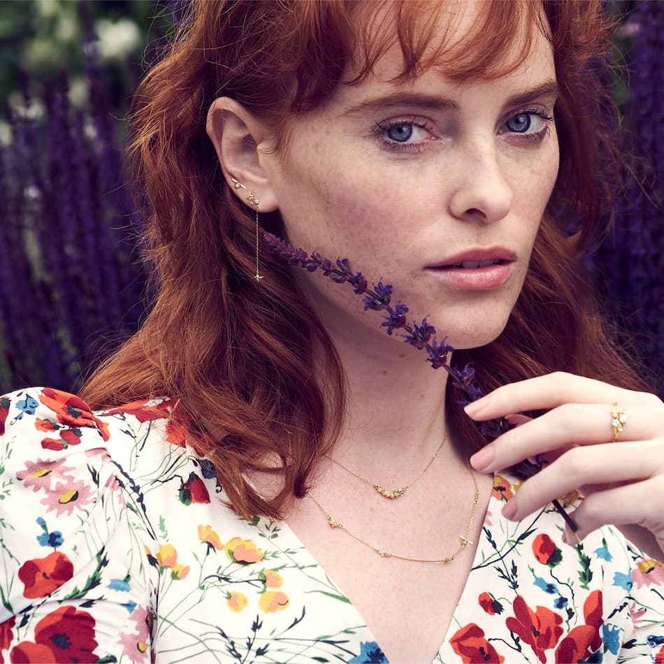 model wearing two 18ct gold necklaces including a plume inline feather necklace and beekeeper fine charm chain by alex monroe