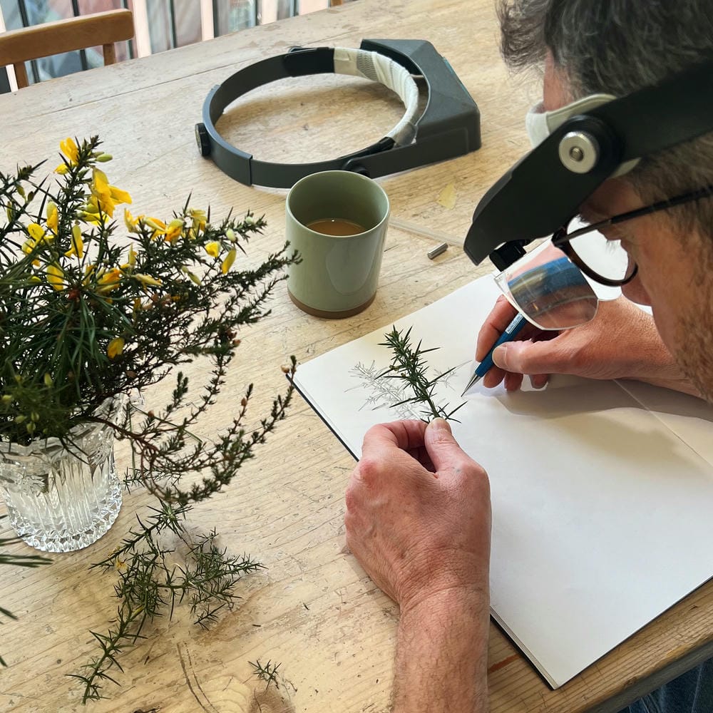 Alex Monroe wearing optivisors and sketching from branches of collected plants.