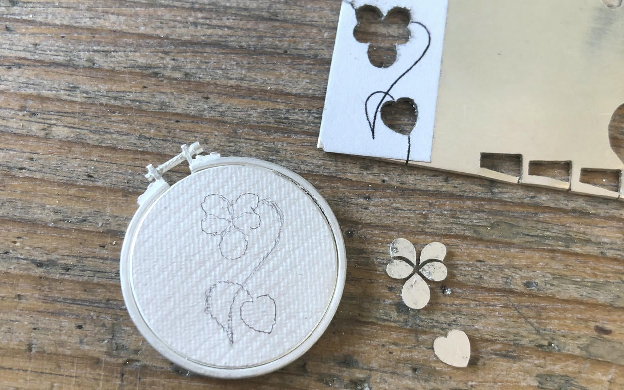 Sheet of silver with shapes cutout and silver sewing circle shape being made.