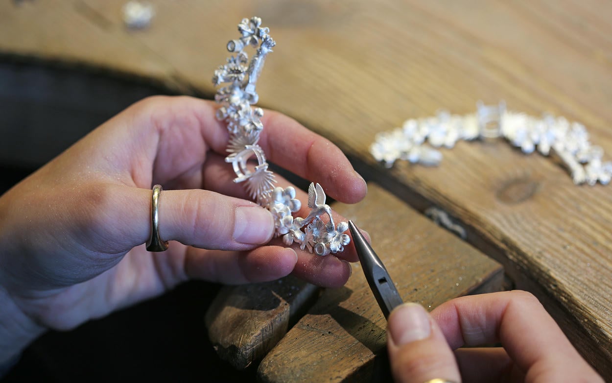 A large silver construction of charms being worked on by a jeweller at a workbench